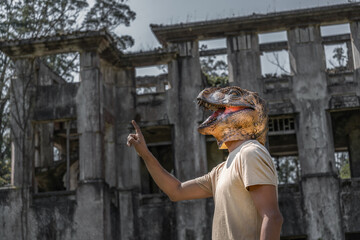 Man in dinosaur mask pointing to copy space in front of horror abandoned house.