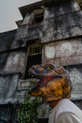 Unrecognizable dinosaur head mask against horror ruined abandoned house