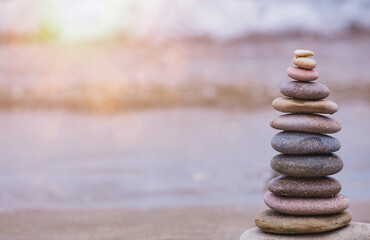 Fototapeta na wymiar Rock balancing or stone stacking, rock stone or sea pebbles pile or pyramid on sand symbolizing zen, harmony, balance. Ocean water and sunset on background. Relaxation concept. Empty space for text.