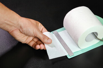 Roll of toilet paper in holder, hand pulls part, on black background close-up