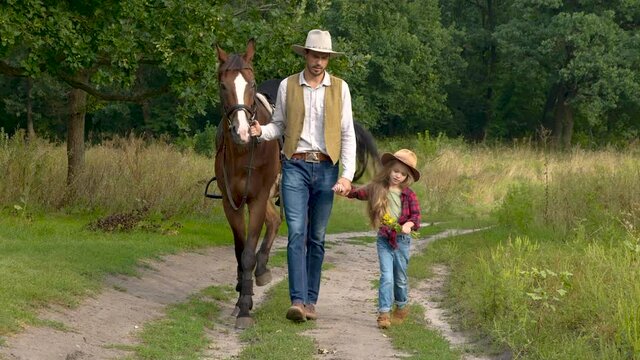 Cowboy with his daughter walking with a horse on a forest road