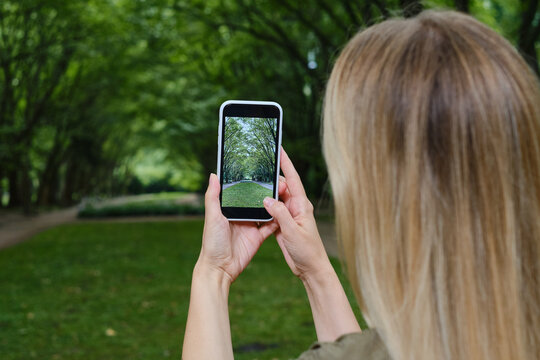 Girl holds a mobile phone in her hands and takes pictures of nature in the park to share photos on social networks. Focus on the phone screen. Make memories using your smartphone. Mobile phone closeup