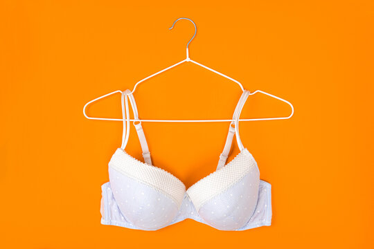 Top view of stylish women bra on white hanger on orange background with copy space. Women's wardrobe