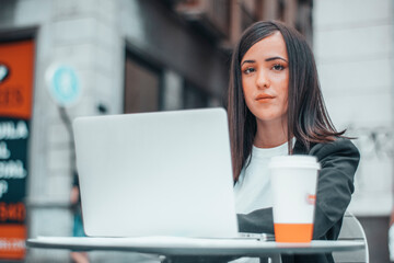 Mujer joven de pelo castaño empresaria tomando un café en la cafeteria de la ciudad con una sonrisa junto a su laptop preparando su trabajo para la empresa