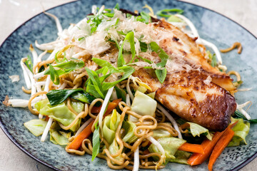 Traditional Japanese fish teriyaki with yakisoba noodles and vegetable served as close-up on a...