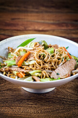 Traditional Japanese pork teriyaki with yakisoba noodles and vegetable served as close-up in a design bowl