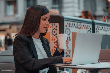 Muchacha joven empresaria revisando su laptop trabajando mientras sostiene su vaso de café por la...