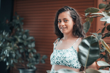 Muchacha joven de pelo castaño sonriendo con emoción y una mirada detrás de las hojas de las plantas en un centro comercial