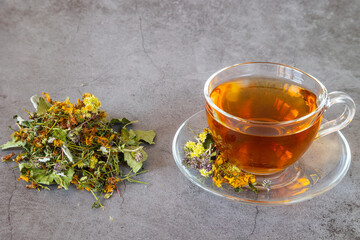 Cup of herbal tea with natural dried herbs on gray background.