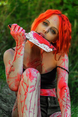 Red-haired woman with bloody knife on a background of greenery - 456808266