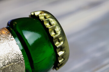 Makro closeup of green beer bottle neck with golden crown cap and foil, white wood background
