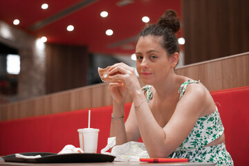Mujer feliz tomando su almuerzo mientras come una hamburguesa con papas fritas y bebe de su gaseosa...