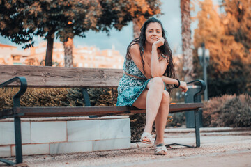 Muchacha adolescente de pelo negro sentada en un banco de un parque con interés mientras observa...