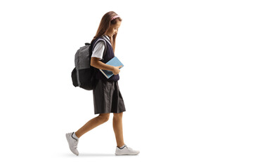 Full length profile shot of a sad female pupil in a school uniform walking and holding a book