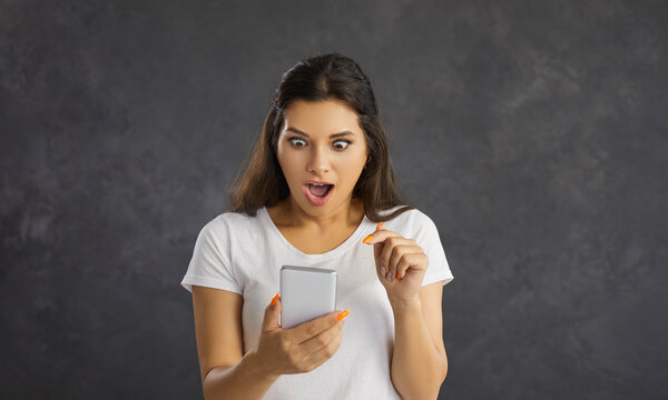 Stunned millennial Hispanic woman on black studio background shocked by news on cellphone. Amazed Latino girl look at smartphone screen surprised by online sale promotion or discount deal.