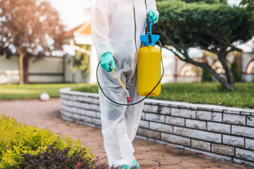 Exterminator in work wear outdoors spraying pesticide with sprayer.