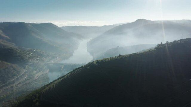 Panoramic view of hilly mountains in morning light, Peso da Regua, Vila Real, Portugal, Europe. Drone shot of sun rays shining Douro valley with vineyards growing on banks of river, 4k footage