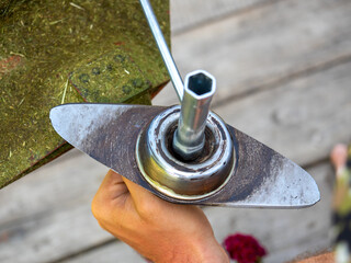 A man uses a key to unscrew the blade on the head of a gasoline trimmer. Close-up, a man at work