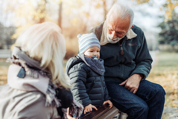 Happy good looking senior couple husband and wife walking and playing with their adorable grandson...