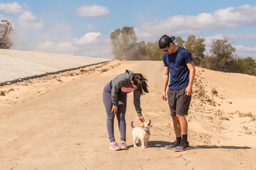Fitness woman with her partner petting her small dog in the sand.