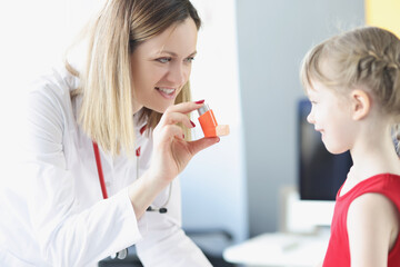 Pulmonologist doctor holding hormonal inhaler in front of little girl in clinic. - obrazy, fototapety, plakaty