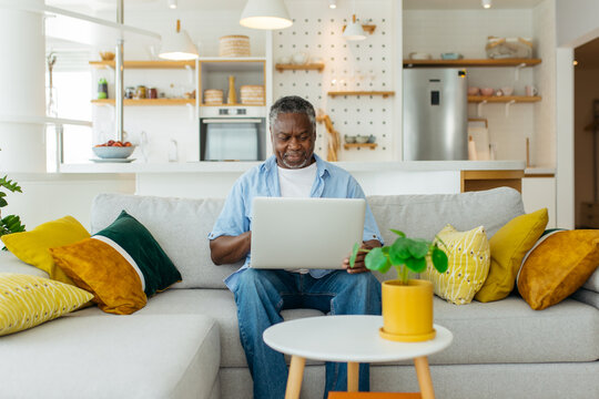 Handsome senior African man sitting on the comfortable sofa and using laptop