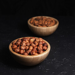 Wooden bowl with pile of hazelnuts placed on black table in studio. Concept of nutritious healthy nut snack 