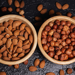 From above of wooden bowls with heaps of hazelnut and almond on black table with scattered nuts in studio 