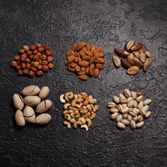 Piles of assorted nuts like pistachio, cashew, almond, hazelnut, Brazilian nut and pecan placed in even rows on black background 