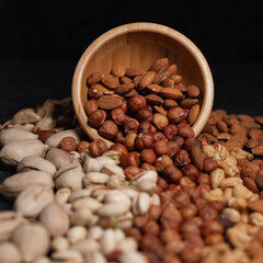 Assorted types of nuts scattering from wooden bowl on black table in studio 