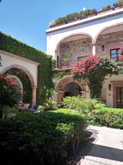 Beautiful old colonial style building filled with plants and flowers with a stone fountain
