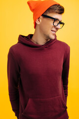 portrait of a handsome guy in an orange hat, red sweater and glasses, on a yellow background, smiling broadly
