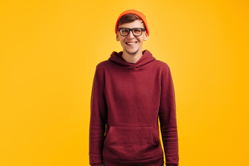 portrait of a handsome guy in an orange hat, red sweater and glasses, on a yellow background, smiling broadly