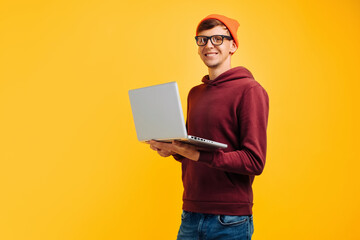 young handsome guy with typing on a laptop, in an orange hat with glasses and a red sweater, on a...