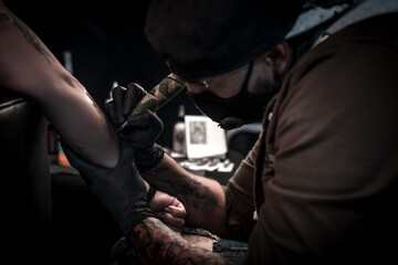 Fototapeta na wymiar A professional tattoo artist makes a tattoo on a woman's hand.