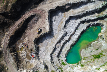 Aggregate mine with heavy machinery, excavators and tipper loaders in aerial shot. Working quarry...