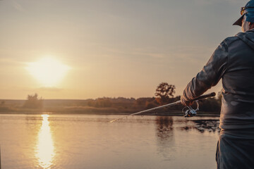 Naklejka premium Fishing rod with a spinning reel in the hands of a fisherman. Fishing background