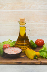 cold-pressed olive oil in a glass bottle with ingredients for cooking summer salad, fresh vegetables tomatoes, cucumbers, bell pepper and green leaf lettuce, pink mineral  himalayan salt seasoning 