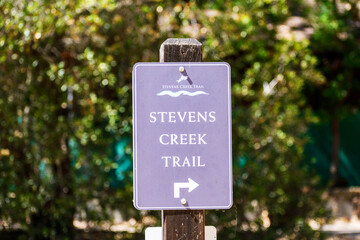 Stevens Creek Trail direction sign in San Francisco Bay Area. Blurred green trees background. -...