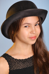 Close-up portrait of a bright cute dark-haired teenage girl 12 years old in a black bowler hat, she looks her brown eyes eye to eye.