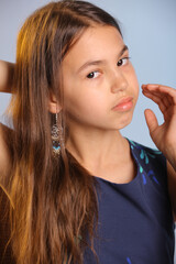 Close-up portrait with hand near face. The portrait shows a beautiful dark-haired teenage girl 12 years old in a blue dress. She looks carefully eye to eye.