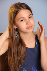 Obraz premium Close-up portrait with hand near face. The portrait shows a beautiful dark-haired teenage girl 12 years old in a blue dress. She looks carefully eye to eye.