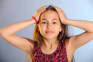 Portrait of a bright cute dark-haired teenage girl 12 years old in a purple dress, she is holding her head with her hands.