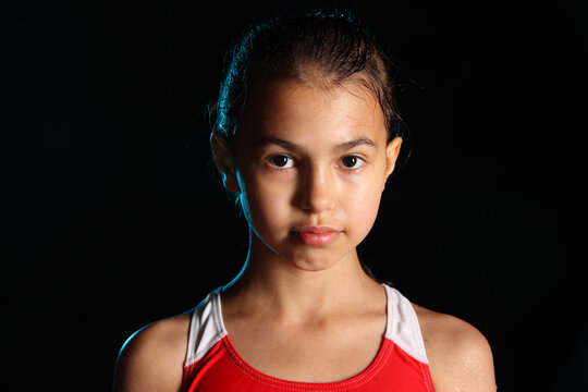 Close-up portrait of a bright beautiful girl swimmer 12 years old on a black background. She has slicked hair and looks eye to eye.