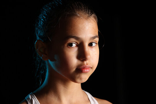 Close-up portrait of a bright beautiful girl swimmer 12 years old on a black background. She has slicked hair and looks eye to eye.
