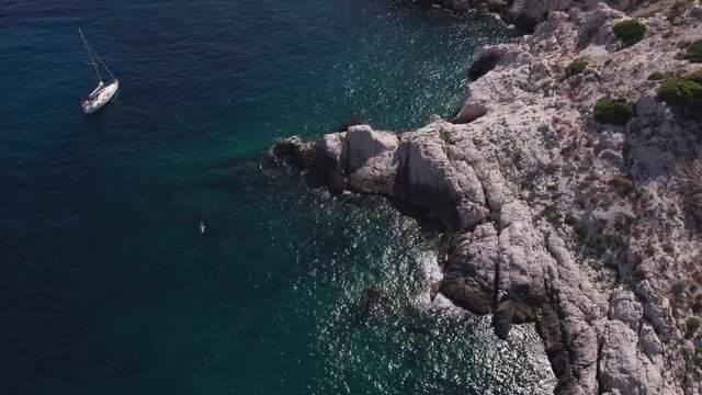 Aerial shot of a drone flying backwards revealing the crystalline waters where sailing boats stopped to relax in the coast of Frioul islands, Marseille.