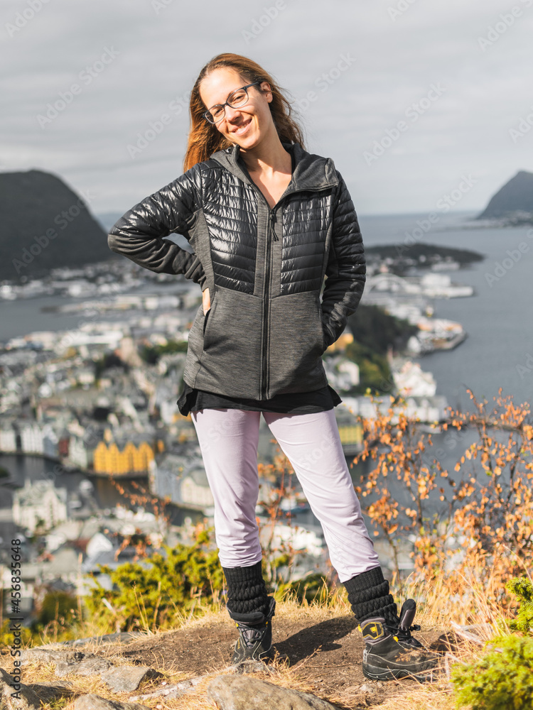 Poster Caucasian woman with long hair wearing glasses and posing in front of the city of Alesund, Norway