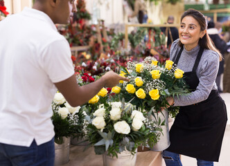 Experienced woman florist helping male client to choose flowers in flower shop