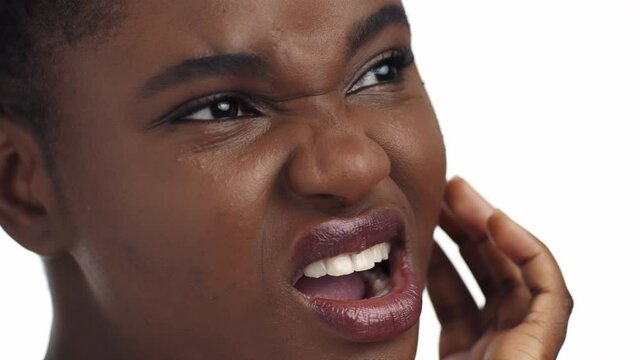 Despaired young african american woman enduring tooth pain, touching her inflamed cheek, close up portrait, slow motion