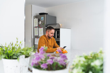 Caucasian male dressed in an orange sweater using his smart phone in a kitchen